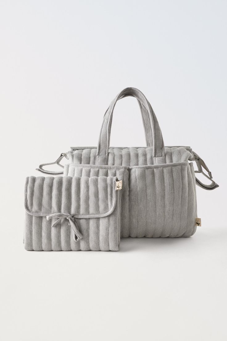 two grey bags sitting next to each other on a white surface with one bag in the middle