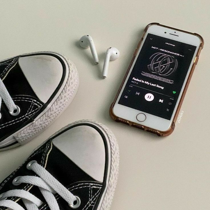 an iphone with ear buds and headphones next to it on a white table top