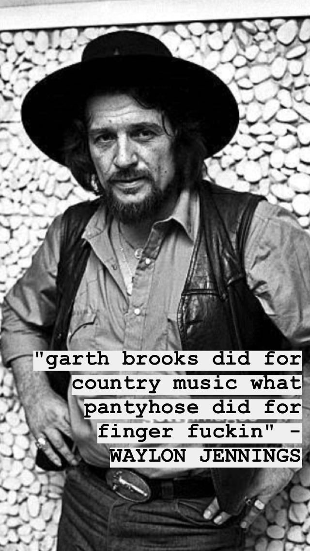 a man wearing a cowboy hat standing in front of a rock wall with a quote on it