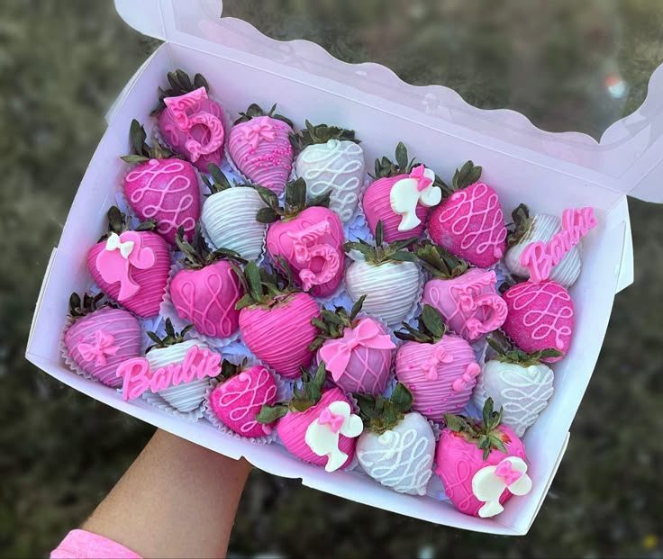 a person holding up a box full of chocolate covered strawberries with pink icing