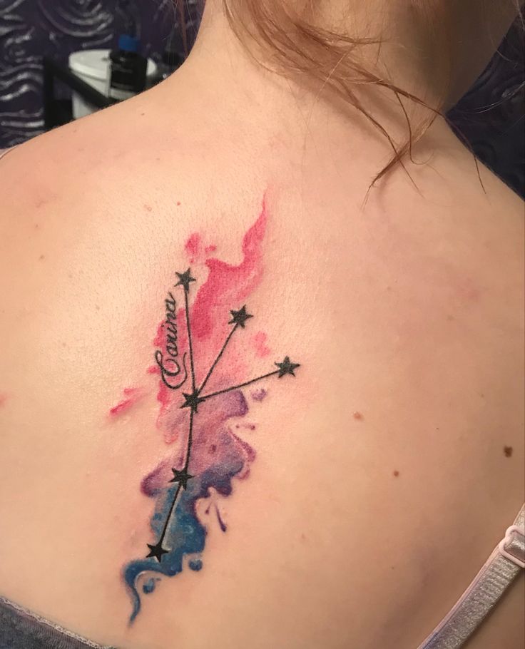 a woman's upper back tattoo with watercolor splashs and stars on it