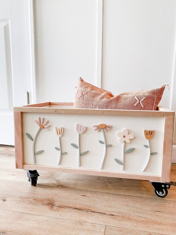 a wooden box with flowers on it and a pillow in the middle, sitting on top of a hard wood floor