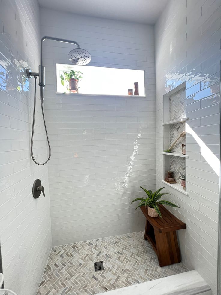 a white tiled bathroom with a wooden bench and shower head mounted to the side of the wall