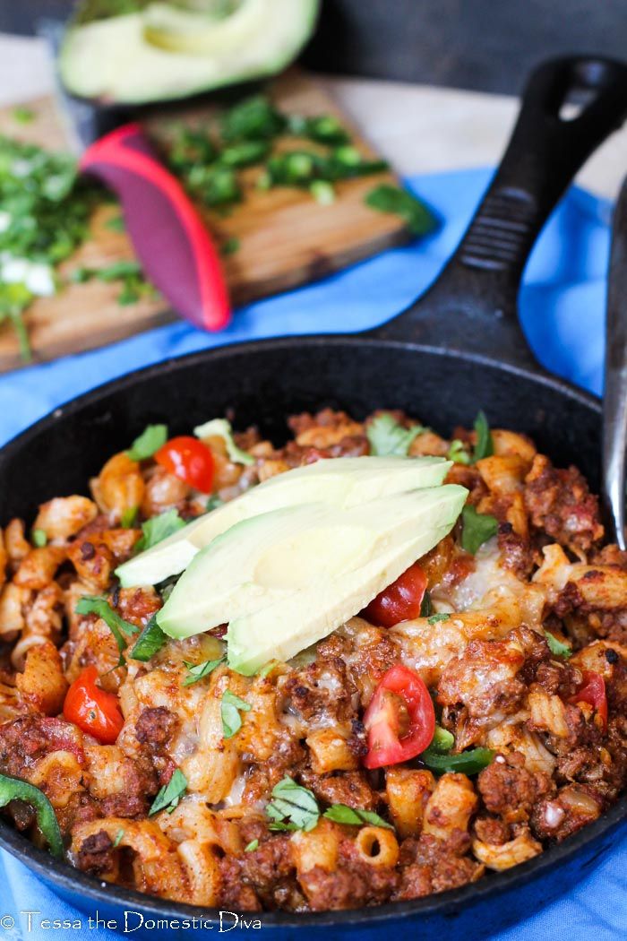 a skillet filled with macaroni and cheese topped with an avocado