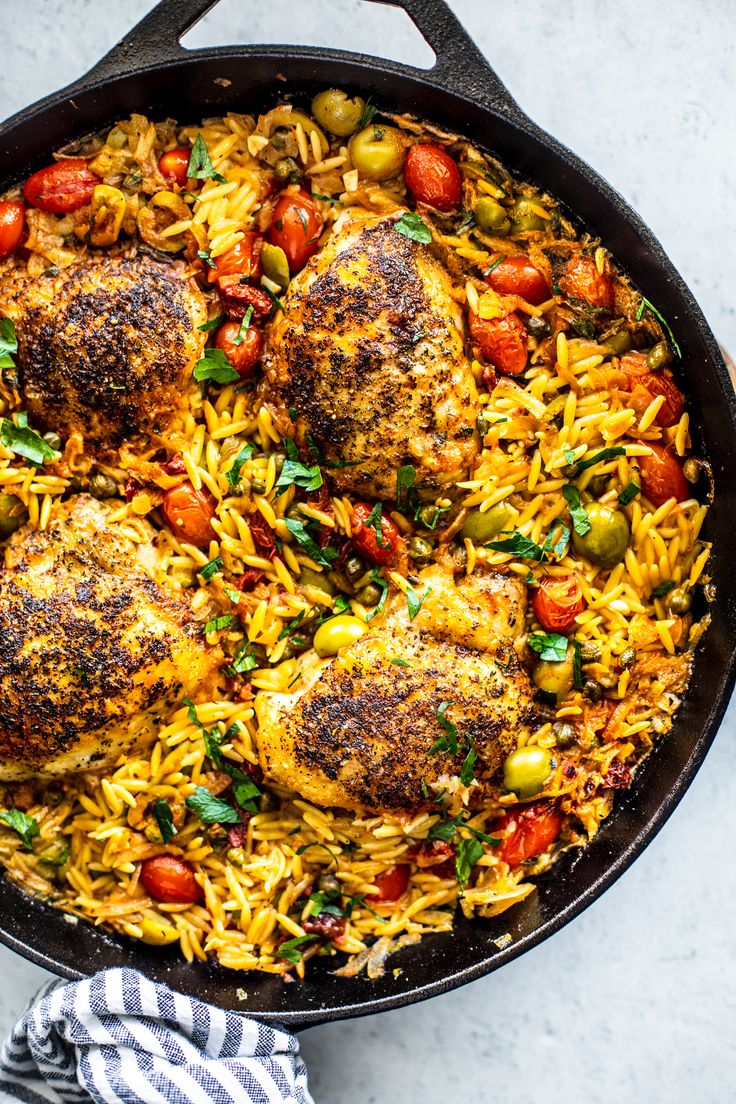 a skillet filled with chicken, rice and tomatoes