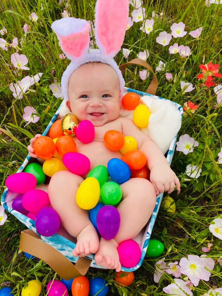 a baby wearing bunny ears laying in the grass with easter eggs