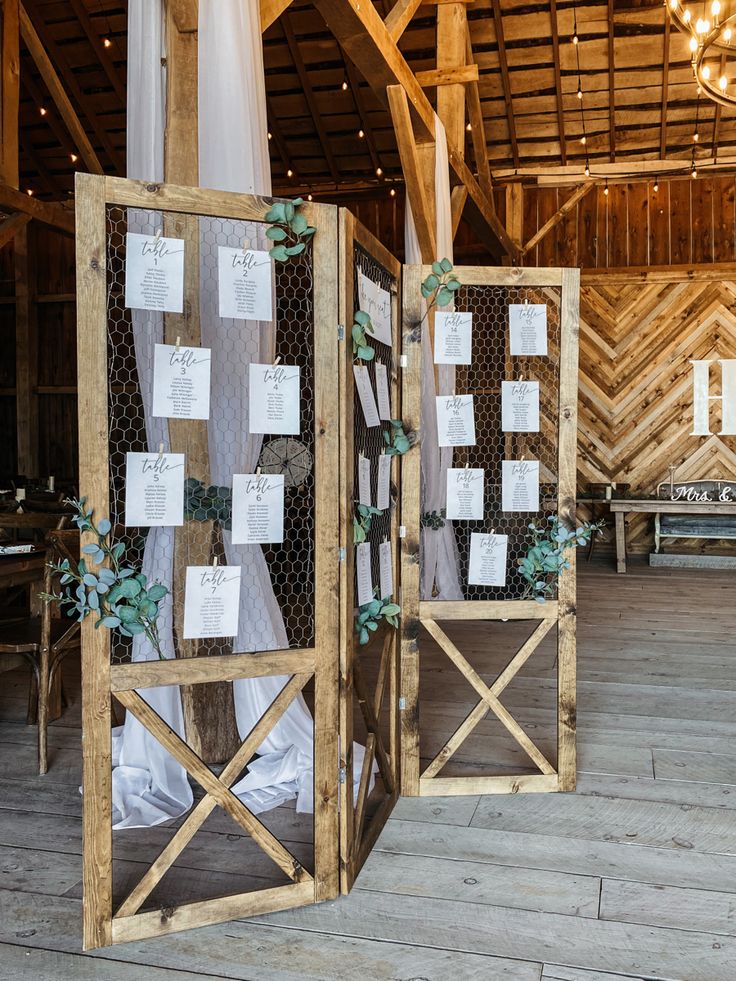 two wooden partitions with seating cards attached to them in an indoor barn wedding venue