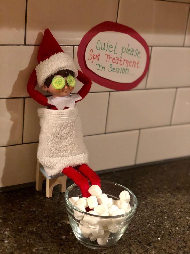 an elf is sitting on top of a bowl of marshmallows and holding a sign that says quiet please spa treatment in session