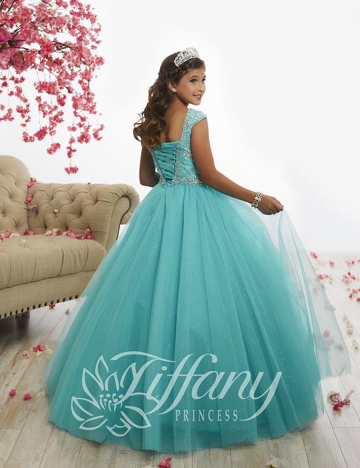 Your sweet girl will love twirling around in this beaded long cap-sleeve dress with an A-line skirt by Tiffany Princess 13521. We adore this off-the-shoulder, rounded neckline dress with a beaded appliqué bodice, full tulle skirt, and lace-up back. House of Wu Tiffany Princess Collection Spring 2018 Style Number: 13521 Fabric: Tulle/Sparkle Tulle Silhouette: Ballgown, A-line Neckline: Scoop Colors: Blue Waterdance Sizes Available (as of 12/26/2023): 4, 6, 8, 10, 12, 14 Occasions: Pageant, Flower Girls Pageant Gowns, Round Neckline Dress, Back House, 2018 Style, Girls Short Dresses, Pageant Gown, Tulle Balls, Full Tulle Skirt, Girls Long Dresses