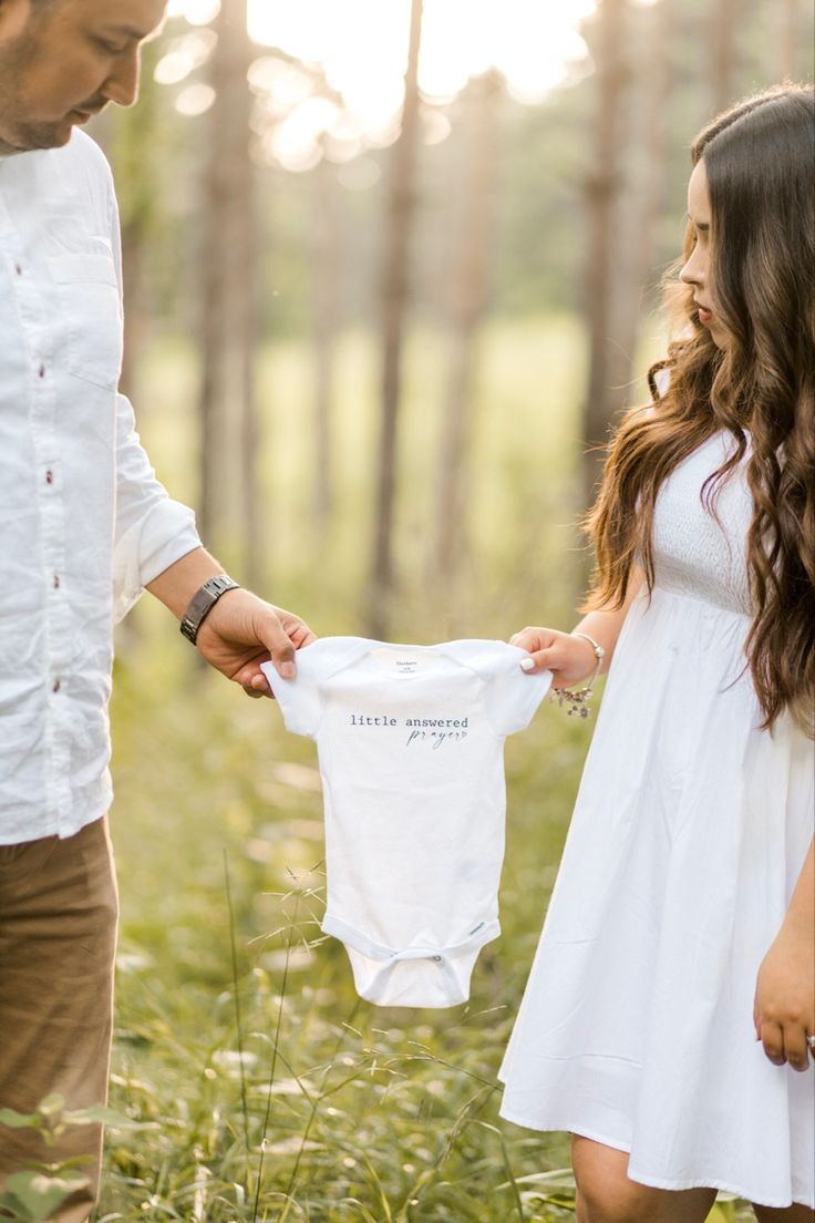 a man holding a baby's shirt while standing next to a woman