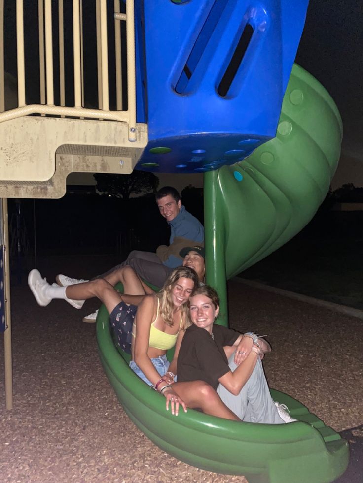 three people are sitting on a green slide