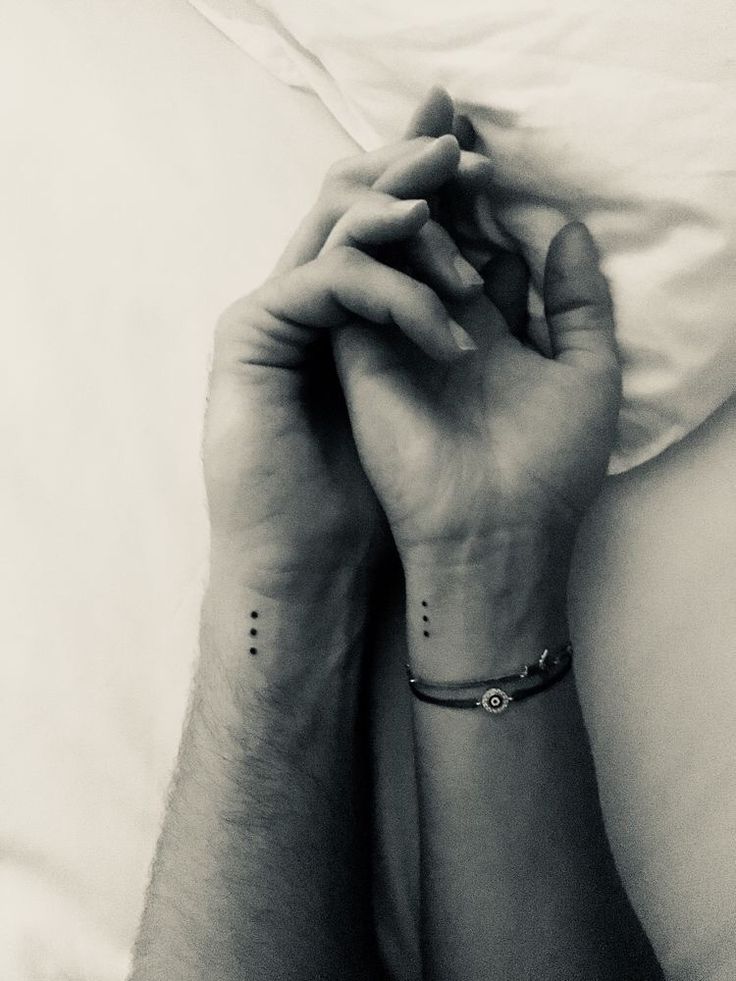 two people with matching tattoos on their arms holding each other's hands in bed