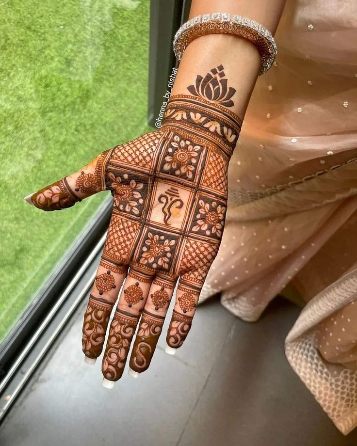 a woman's hand with henna tattoos on it and green grass in the background