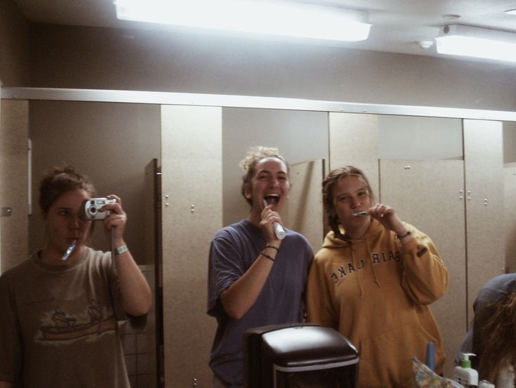 three people standing in front of a mirror brushing their teeth