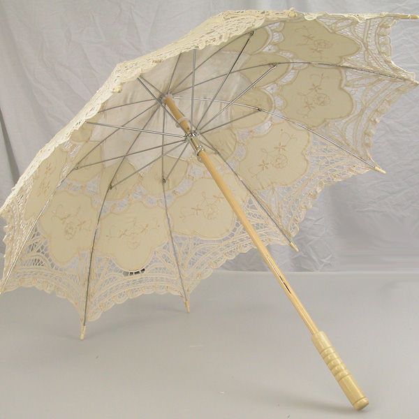 an open lace umbrella with wooden handle on a white tablecloth covered surface, in front of a plain background