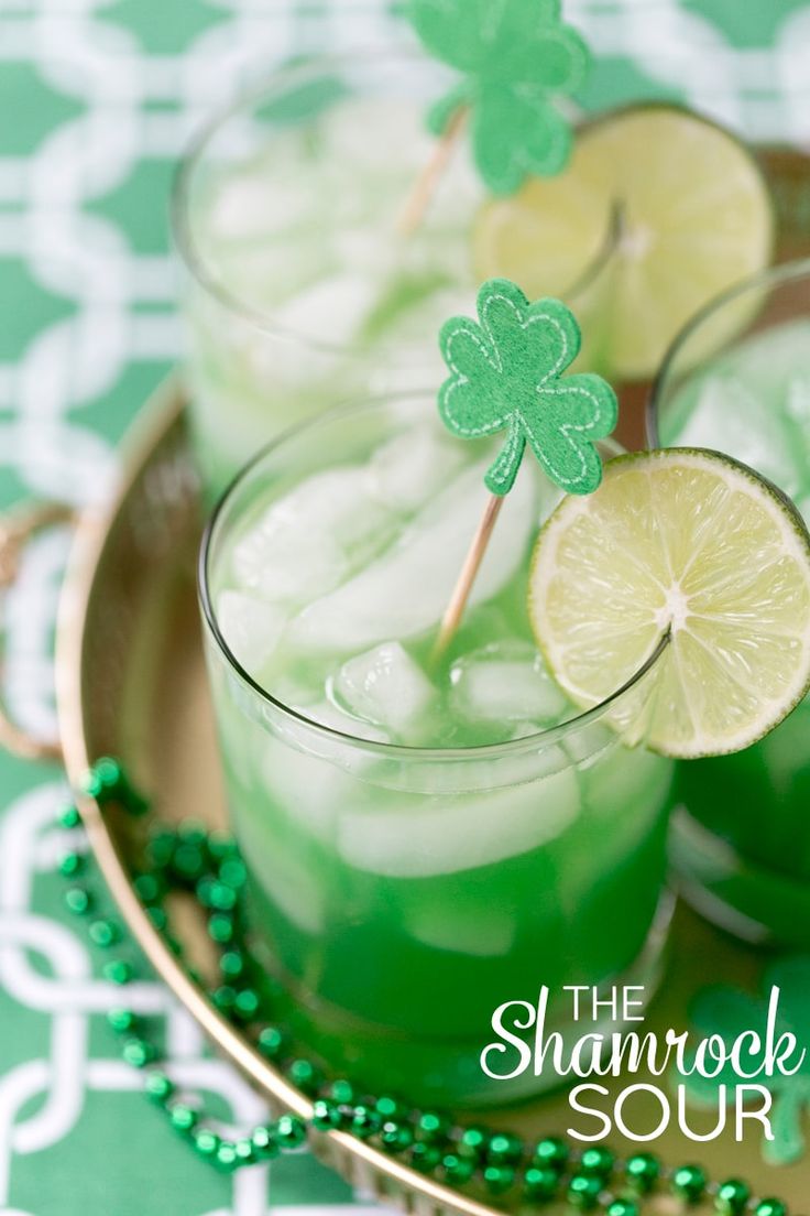 two glasses filled with green liquid and lime slices on top of each other, sitting on a plate