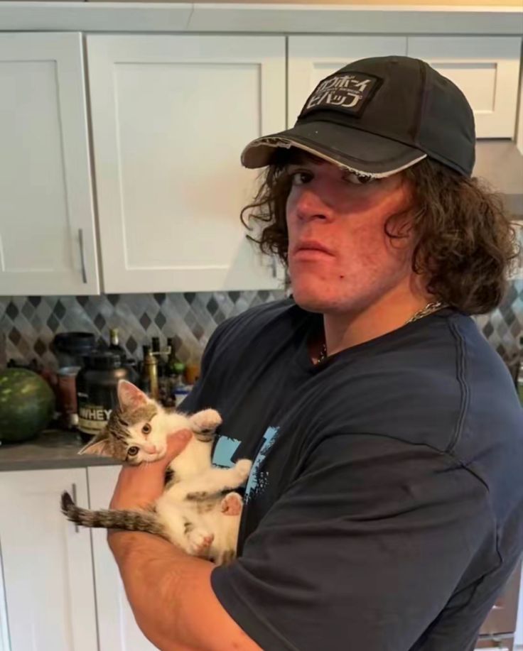 a man holding a cat in his arms and wearing a hat on top of his head