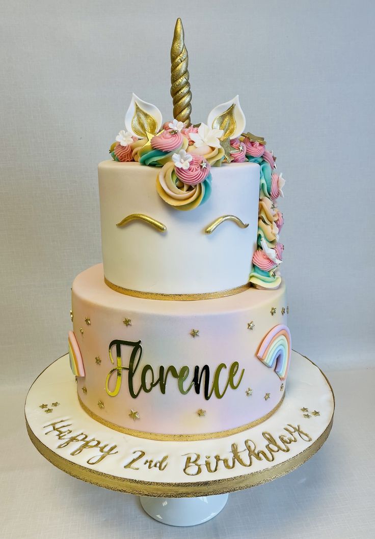 a birthday cake decorated with an unicorn horn and flowers on the top is sitting on a pedestal