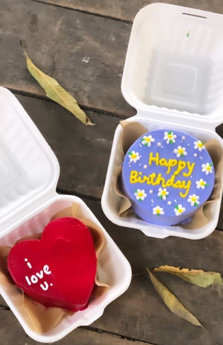 two heart shaped cookies in plastic containers with the words happy birthday written on one of them