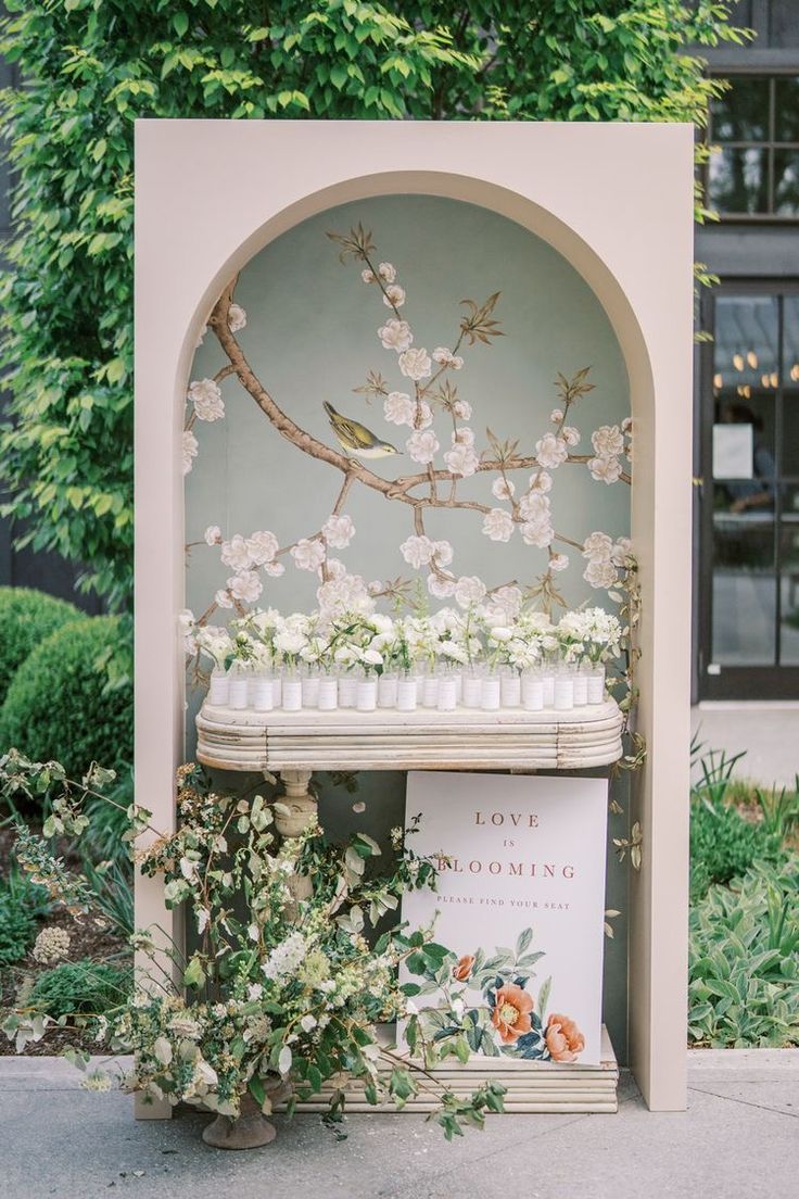 an outdoor display with candles and flowers on the outside wall, along with a sign that says love is blooming