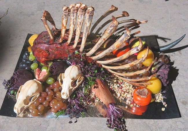 an arrangement of bones, vegetables and meats on a black platter in the shape of a human skeleton