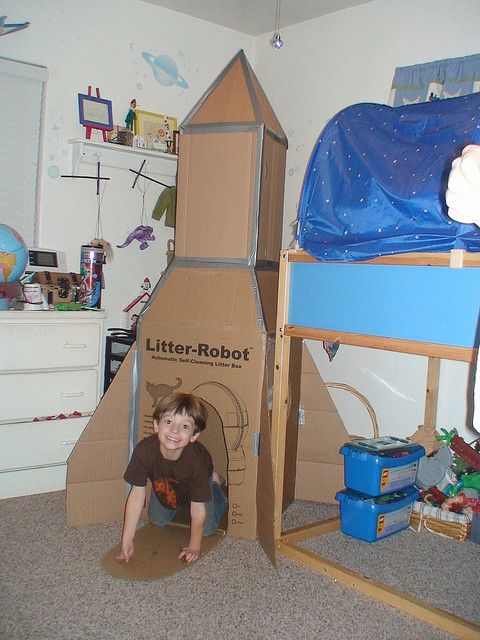 a young boy is playing in a cardboard rocket ship