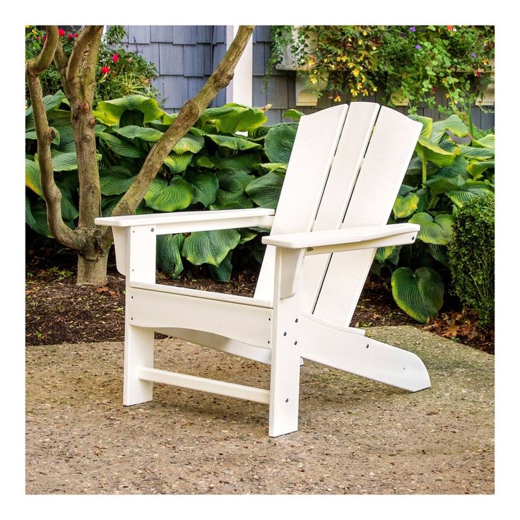 a white adironda chair sitting in front of a tree and shrubbery on the side of a house