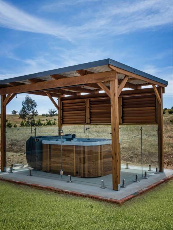 a wooden gazebo with a hot tub in the middle and grass on the ground