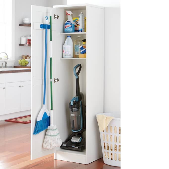 a white cabinet filled with cleaning supplies next to a laundry hamper and mop