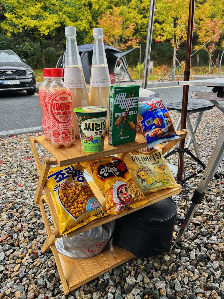 an outdoor picnic table with snacks and drinks on it, next to a car parked in the background