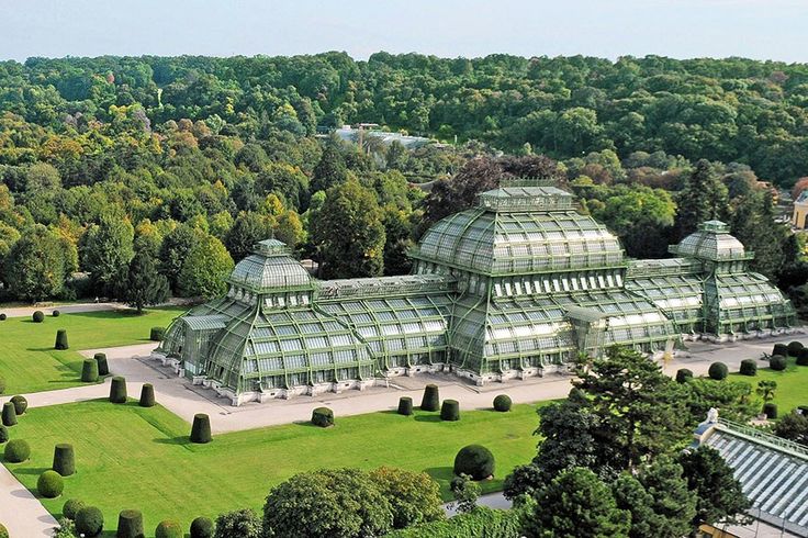 an aerial view of a large glass building in the middle of a green park with lots of trees