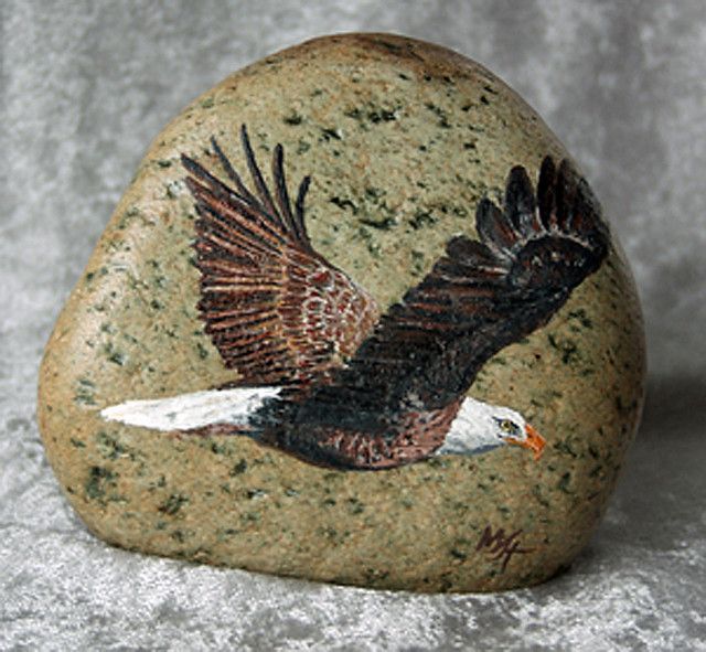 a rock with an eagle painted on it sitting on a white surface next to a gray background