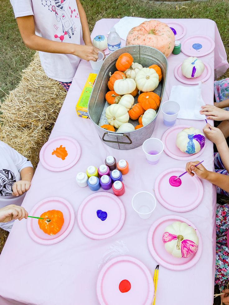 children are painting pumpkins on paper plates at a table with hay and straw bales