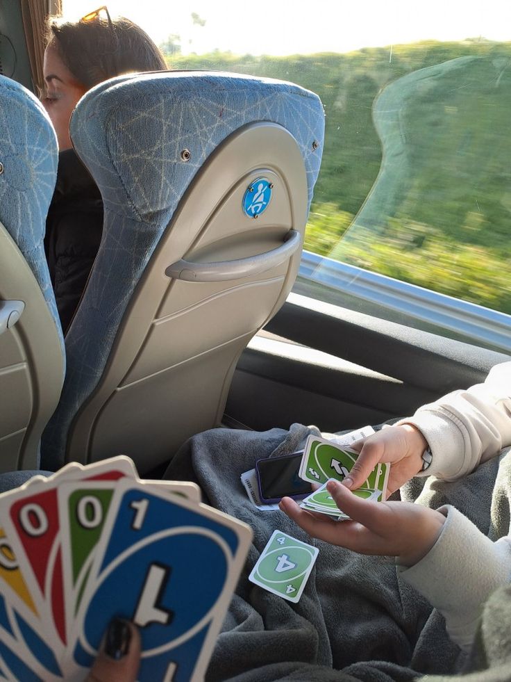 two people playing cards in the back seat of a car while another person looks on