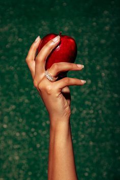 a woman's hand holding an apple in front of a green background with bubbles