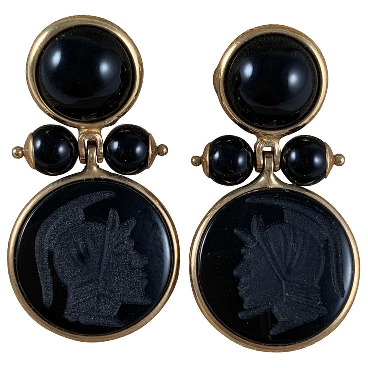 From Italy, a pair of 14-karat gold framed earrings with black onyx cabochons, beads, and carved armorial intaglios. Posted with backs. The upper bezels hold flat back cabochon cut, domed onyx stones, terminating with two pinned and capped onyx beads. The pins hold a swinging, bezeled carved onyx stone, each showing a different Roman helmeted warrior head. Measures: 1 inch Long (25.4 mm) x .75 inch Wide (19.05 mm) .50 inches from front to end of post. Intaglios: .50 inches diameter (12.7 mm) Top Regulus Black, Jeweled Earrings, Onyx Bead, Onyx Stone, Gold Frame, Black Onyx, Onyx, Cufflinks, Gold Jewelry