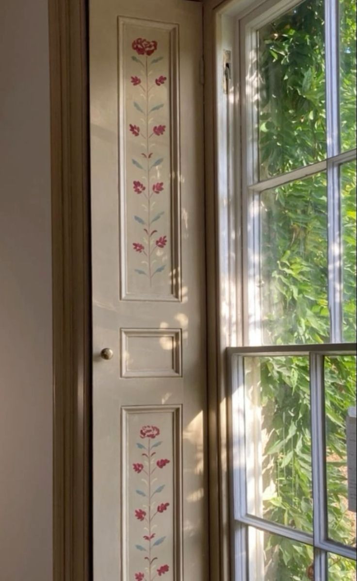 an open door in front of a window with flowers painted on the outside and inside