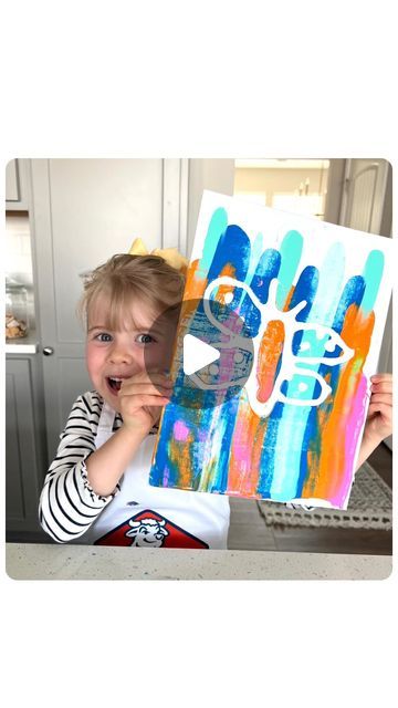 a little boy holding up a painting in front of his face with the word art on it