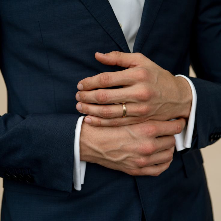 a man in a suit with his hands on his chest and wearing a wedding ring