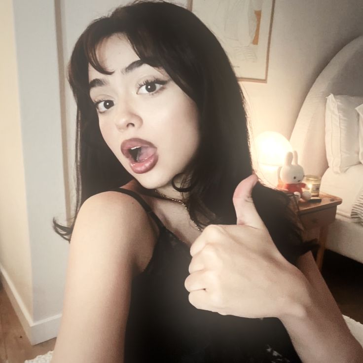 a woman giving the thumbs up sign in her bedroom