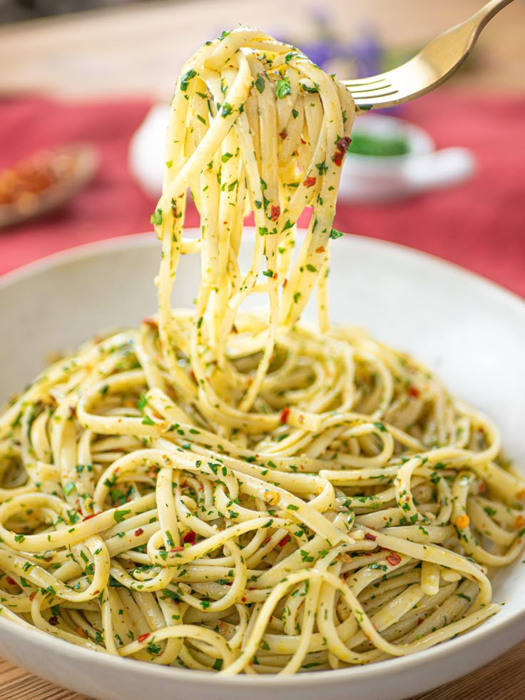 a fork full of spaghetti with parsley sprinkled on it in a white bowl