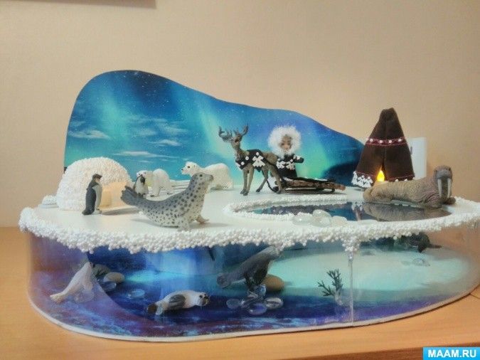 a christmas scene made out of paper with animals and trees in the snow, on top of a wooden table