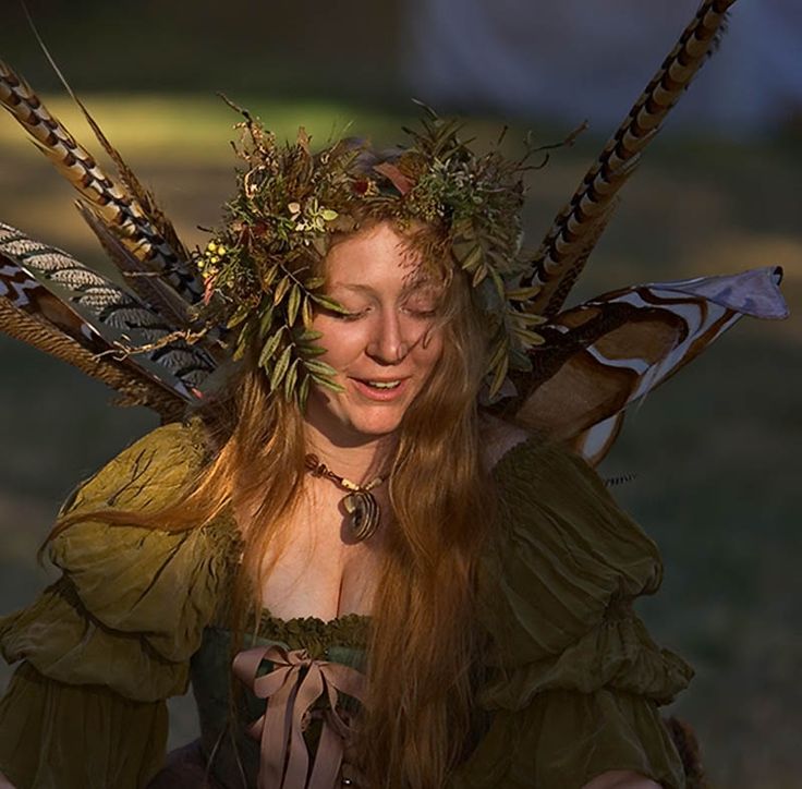 a woman with long red hair is dressed in green and has feathers on her head