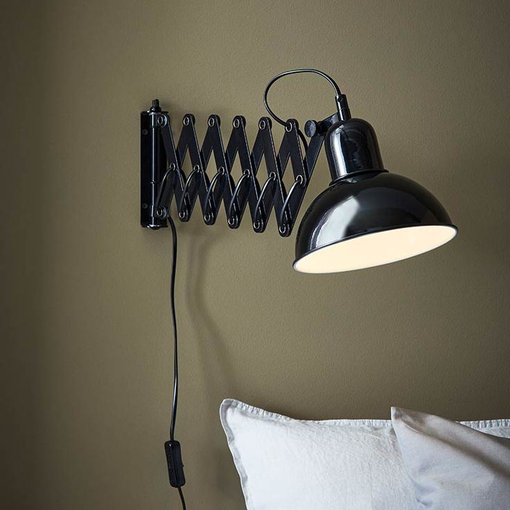 a black lamp on the wall next to a bed with white pillows and a pillow