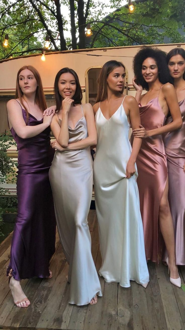 four women in evening dresses posing for a photo on a wooden deck with a trailer behind them