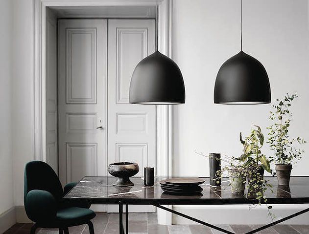 two black lamps hanging over a table with plates and cups on it, next to a potted plant