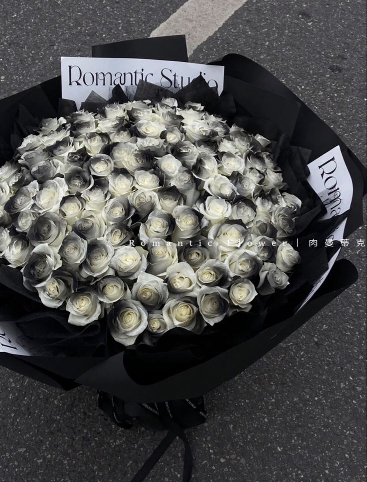 a bouquet of white roses sitting on top of a black wrapper next to a street