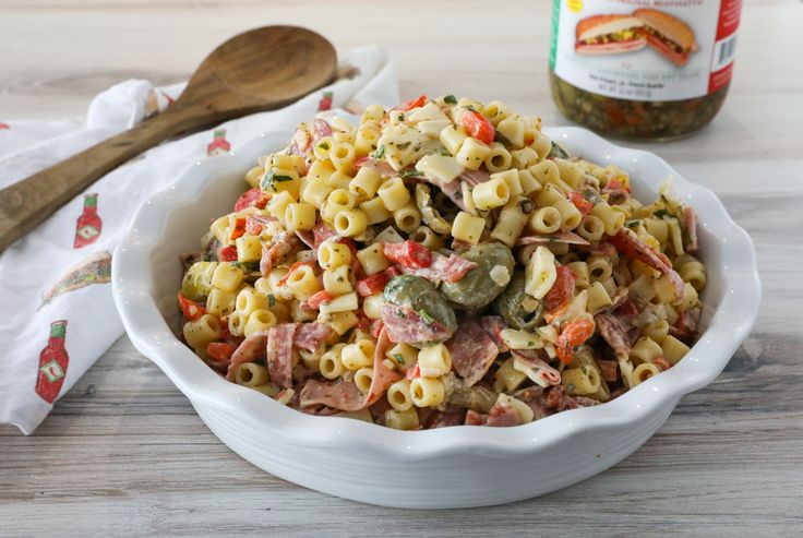 a white bowl filled with pasta salad next to a wooden spoon and jar of seasoning