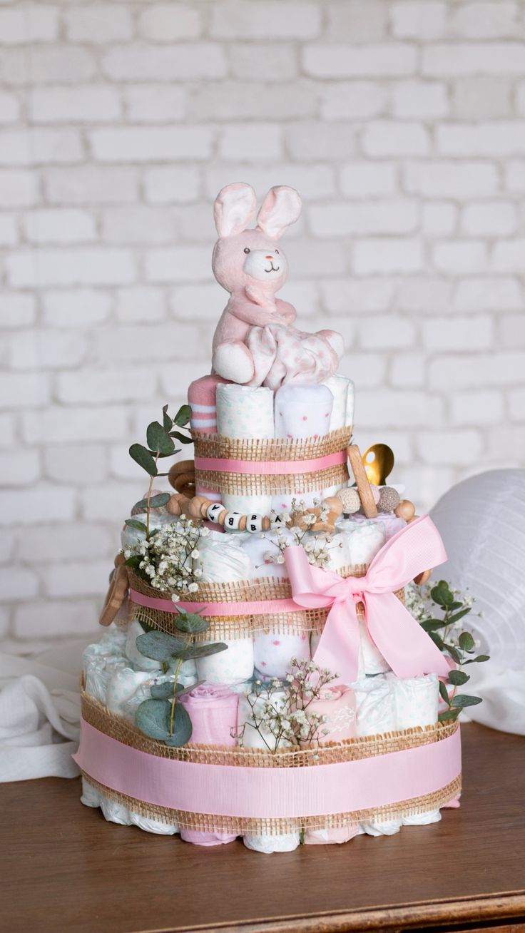 a pink and gold diaper cake on top of a wooden table next to a white brick wall