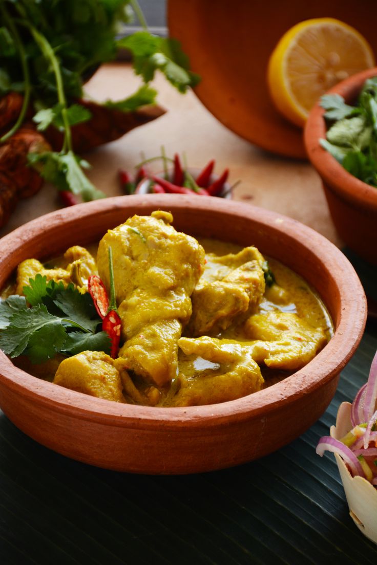 a wooden bowl filled with chicken curry next to other vegetables and herbs on a table